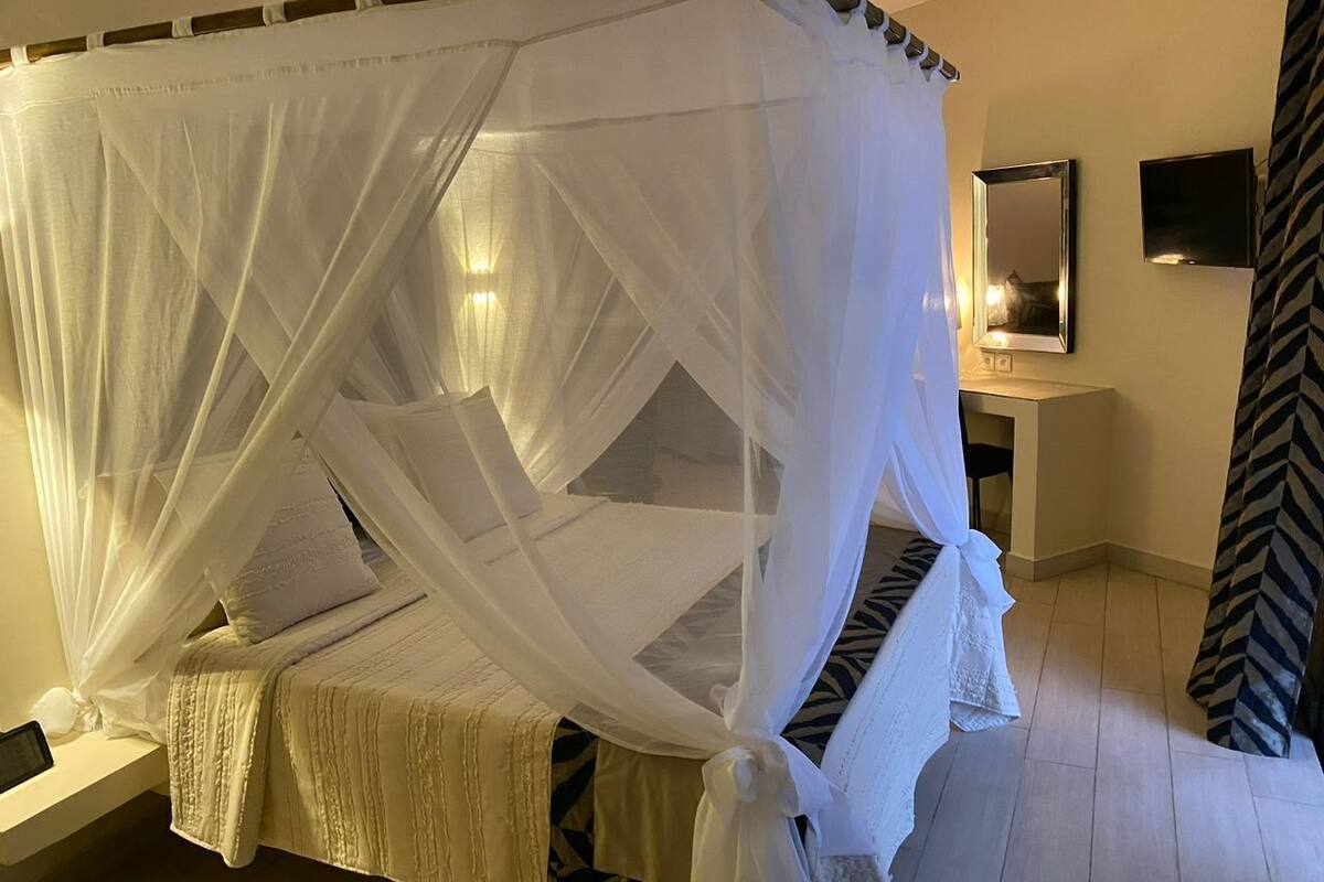 Ein Bett mit weißem Baldachin, ein Nachttisch, ein Spiegel und ein gemustertes Vorhang.