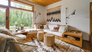 Ein gemütliches Wohnzimmer mit Holzboden, großen Fenstern, einem weißen Sofa und einem rustikalen Teppich.