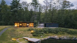 Ein modernes Blockhaus mit Glasfassade, einem Steg und einem kleinen Schuppen, umgeben von Wald und See.
