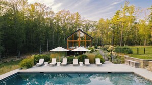 A swimming pool with lounge chairs and umbrellas, surrounded by a forested area. - A Retreat @ Hudson Woods With Pool & Hot Tub (Kerhonkson)