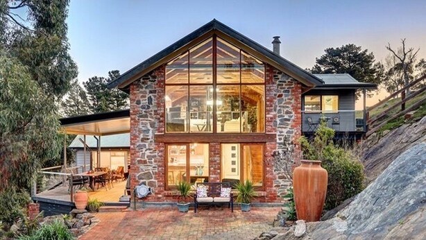 A two-story stone house with large windows, a patio with outdoor furniture, and a stone pathway leading to the entrance.