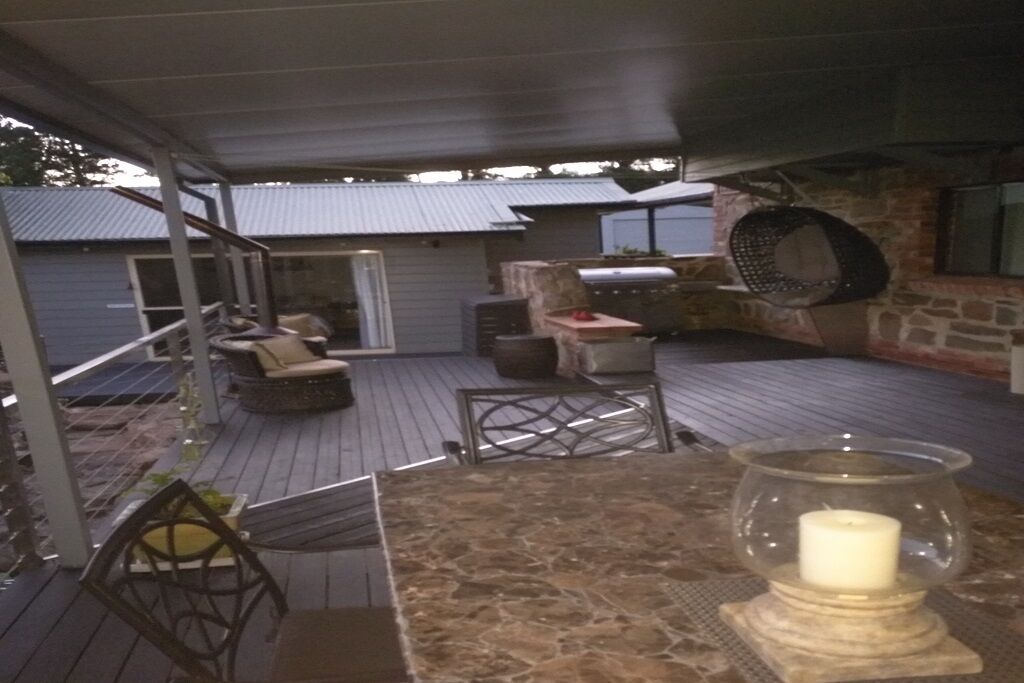 A covered outdoor patio with a stone table, seating, and a grill area.