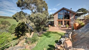 A modern house with a stone facade, large windows, and a well-maintained garden with rocks and a tree.