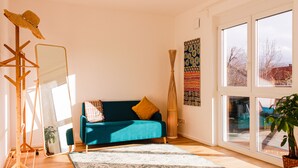 A room with a teal sofa, a large mirror, a hanging light fixture, and a view through large windows.