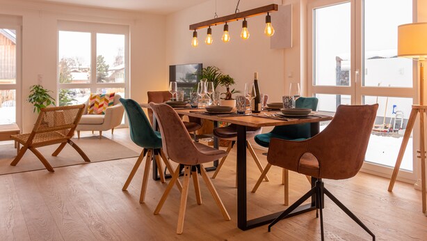 A modern dining area with a wooden table, multiple chairs, and a hanging light fixture.