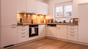 A modern kitchen with white cabinets, wooden countertops, a built-in oven, and a dishwasher.