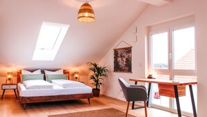 A bedroom with a bed, bedside tables, a desk, a chair, a potted plant, and a window.