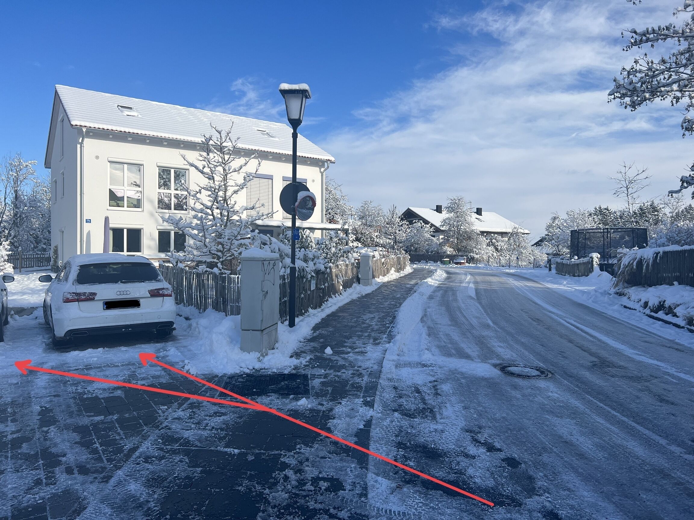 Une rue résidentielle bordée de maisons recouvertes de neige et où une voiture blanche est garée sur le bord.