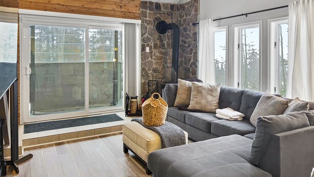 A modern living room with a stone accent wall, a grey sofa, and a large sliding glass door leading to a balcony. - Great views from condo w/free winter shuttle (Brian Head)