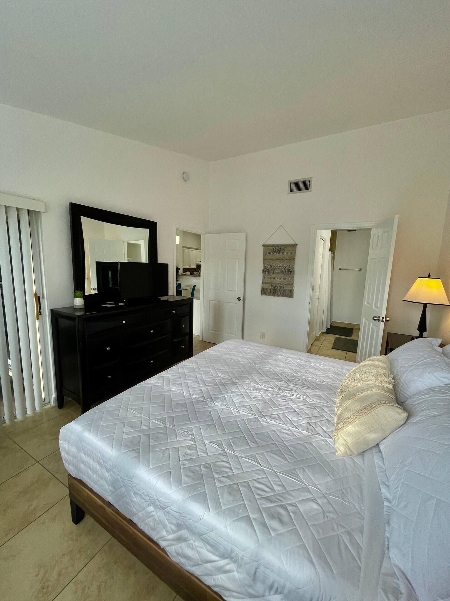 A bedroom with a bed, a dresser, a mirror, and a lamp.