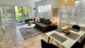 A spacious living area with a sofa, dining table, and chairs, a ceiling fan, and a view of the outdoors. - 340B - Boca Retreat w/ Pool, Parking, Near Evert Tennis & Shops (Boca Raton)