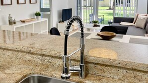 A modern kitchen with a stainless steel sink, a unique faucet, and a large woven pendant light. - 340B - Boca Retreat w/ Pool, Parking, Near Evert Tennis & Shops (Boca Raton)
