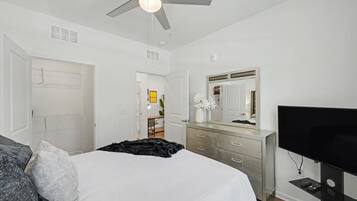 A bedroom with a bed, a dresser, a television, and a ceiling fan.
