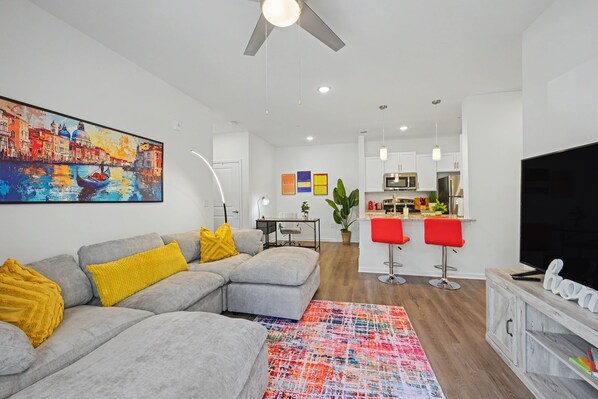 A modern living room with a grey sectional sofa, a colorful abstract painting, and a vibrant rug.