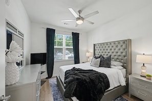Ein Schlafzimmer mit Bett, Nachttischen, Deckenventilator, Fenster mit Vorhängen und einer dekorativen Vase.