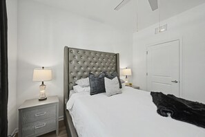 A bedroom with a tufted headboard, a white bedspread, and two bedside tables with lamps.