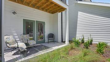 A covered porch with a bench and chairs, a door with a window, and a small garden area with grass and plants.