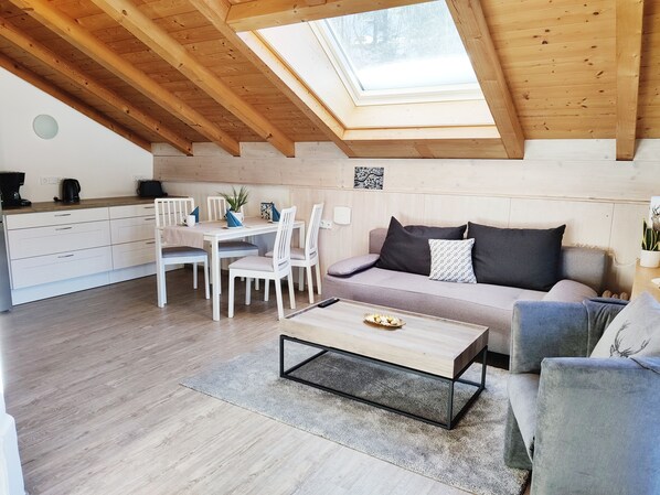 A cozy loft-style living space with a skylight, wooden beams, a dining area, and a sofa with cushions.