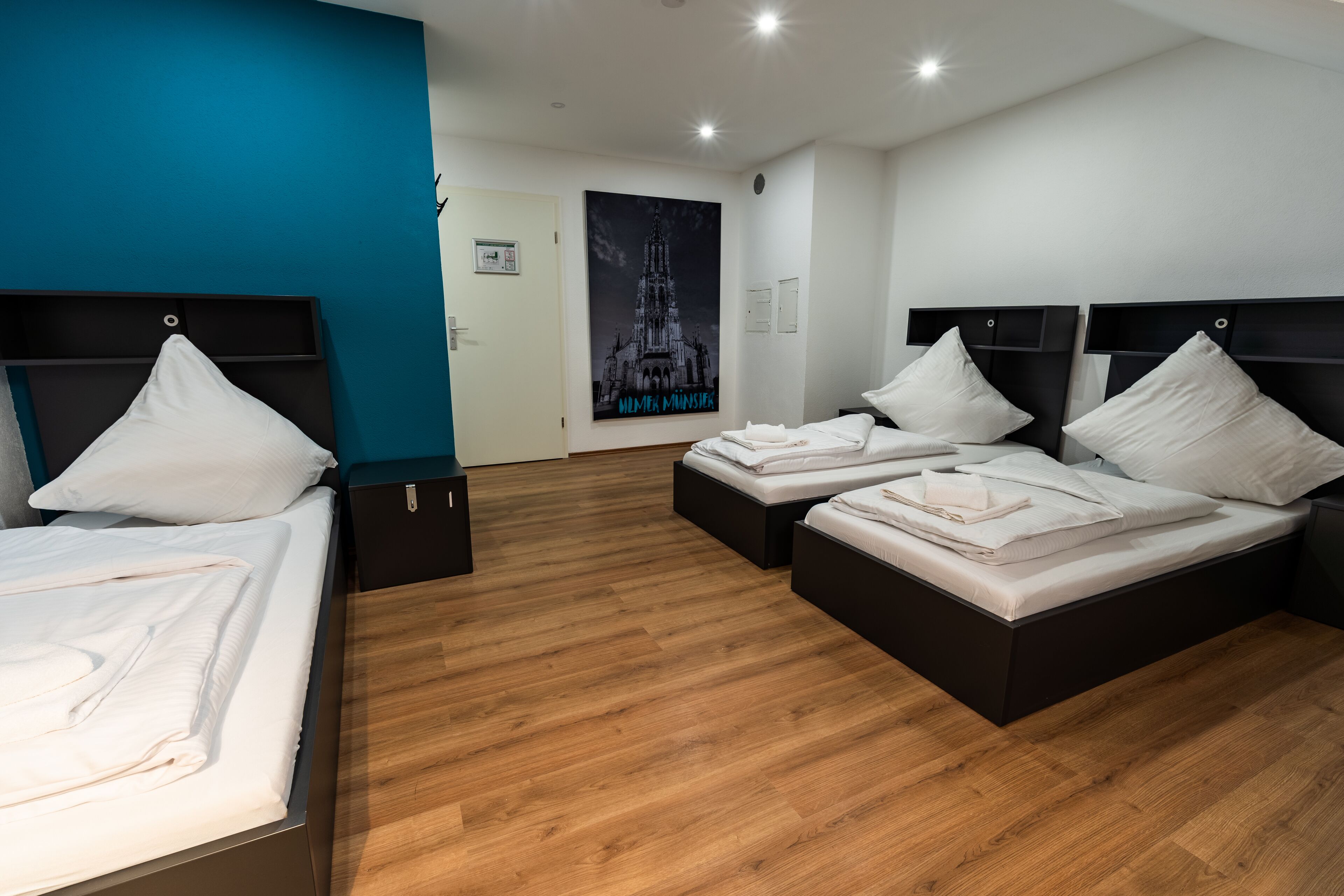 Una habitación de hotel con dos camas individuales, suelo de madera, una pared de acento azul y un cartel con una catedral.