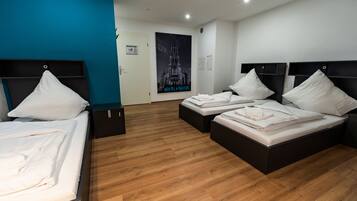 Una habitación de hotel con dos camas individuales, suelo de madera, una pared de acento azul y un cartel con una catedral.