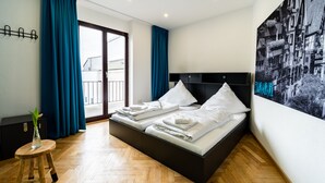 A modern hotel room with a large bed, a view of the city through a glass door, and a large cityscape painting on the wall.
