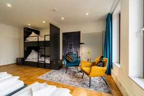 Cozy retreat with a bunk bed, armchairs, and sofa, plus a large window with blue curtains.