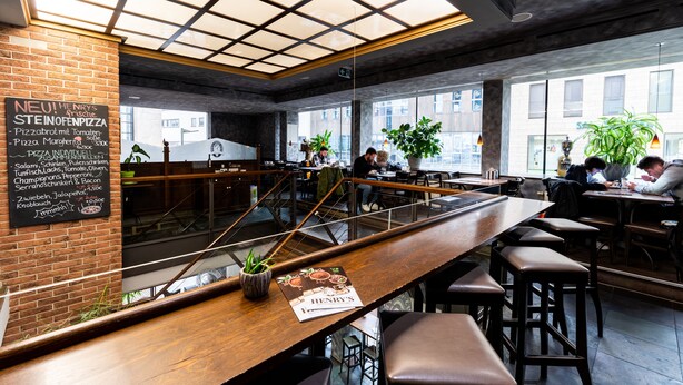 A modern restaurant with a brick wall menu, wooden bar, and seating area.