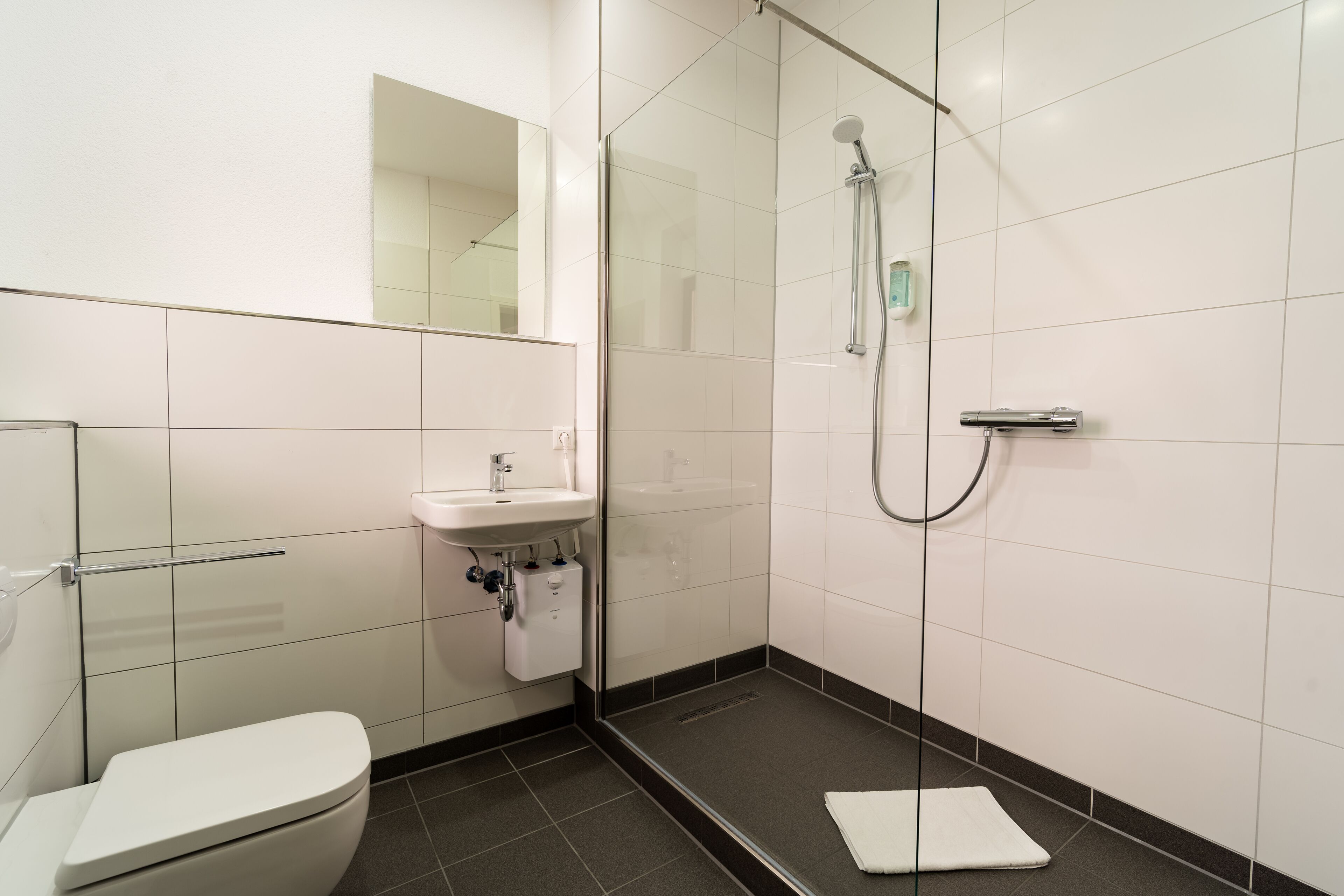 Un baño moderno con inodoro, lavamanos y zona de ducha con mampara de vidrio.