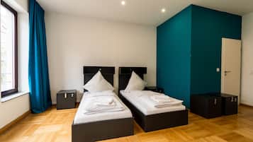 Una habitación de hotel moderna con dos camas, una pared de acento color turquesa y un amplio ventanal con cortinas.