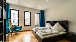 A modern hotel room with two beds, a desk, and a view of the city.