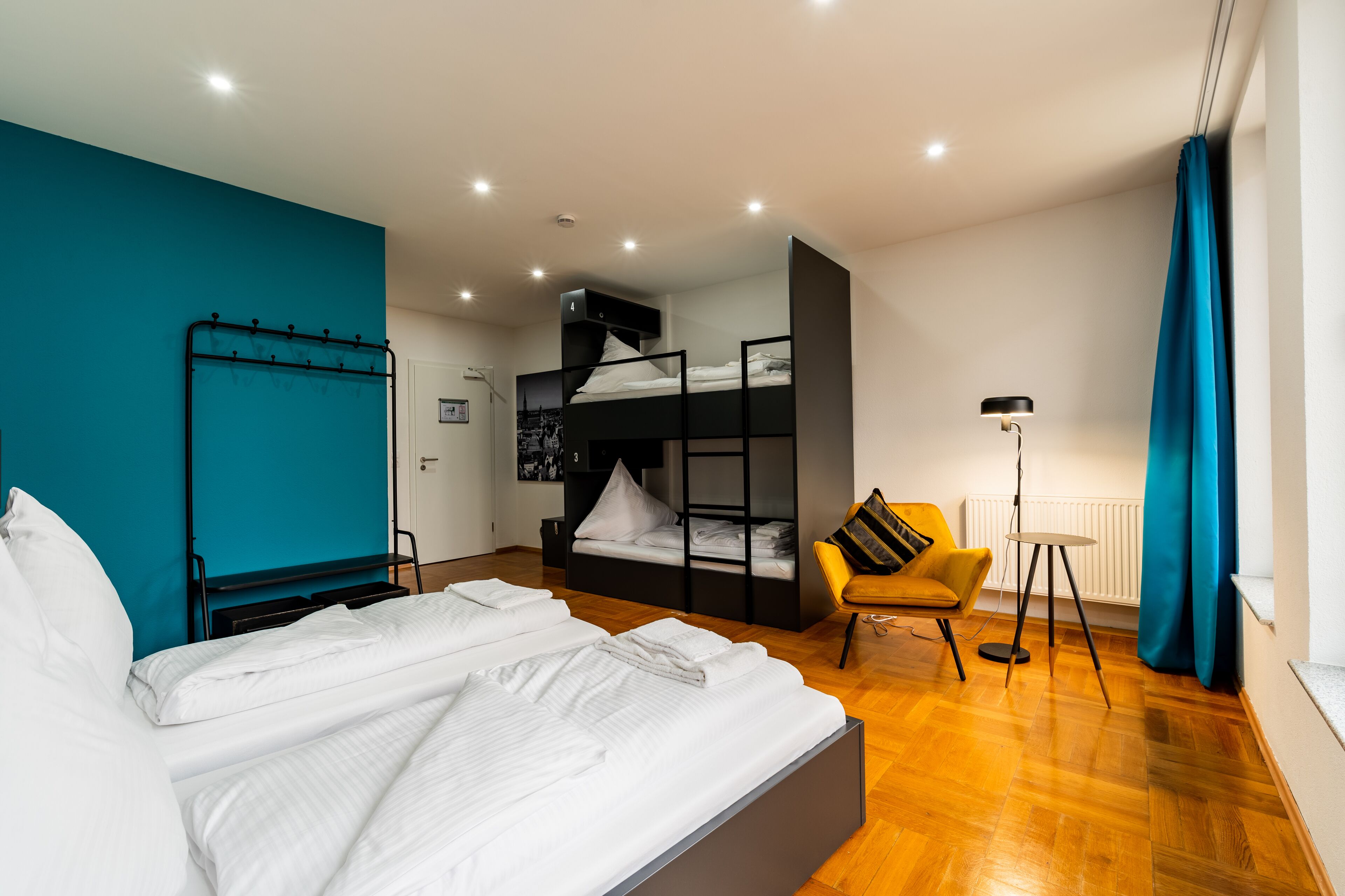 Un dormitorio moderno con una cama grande, una cama literera, un sillón amarillo y una lámpara de pie.