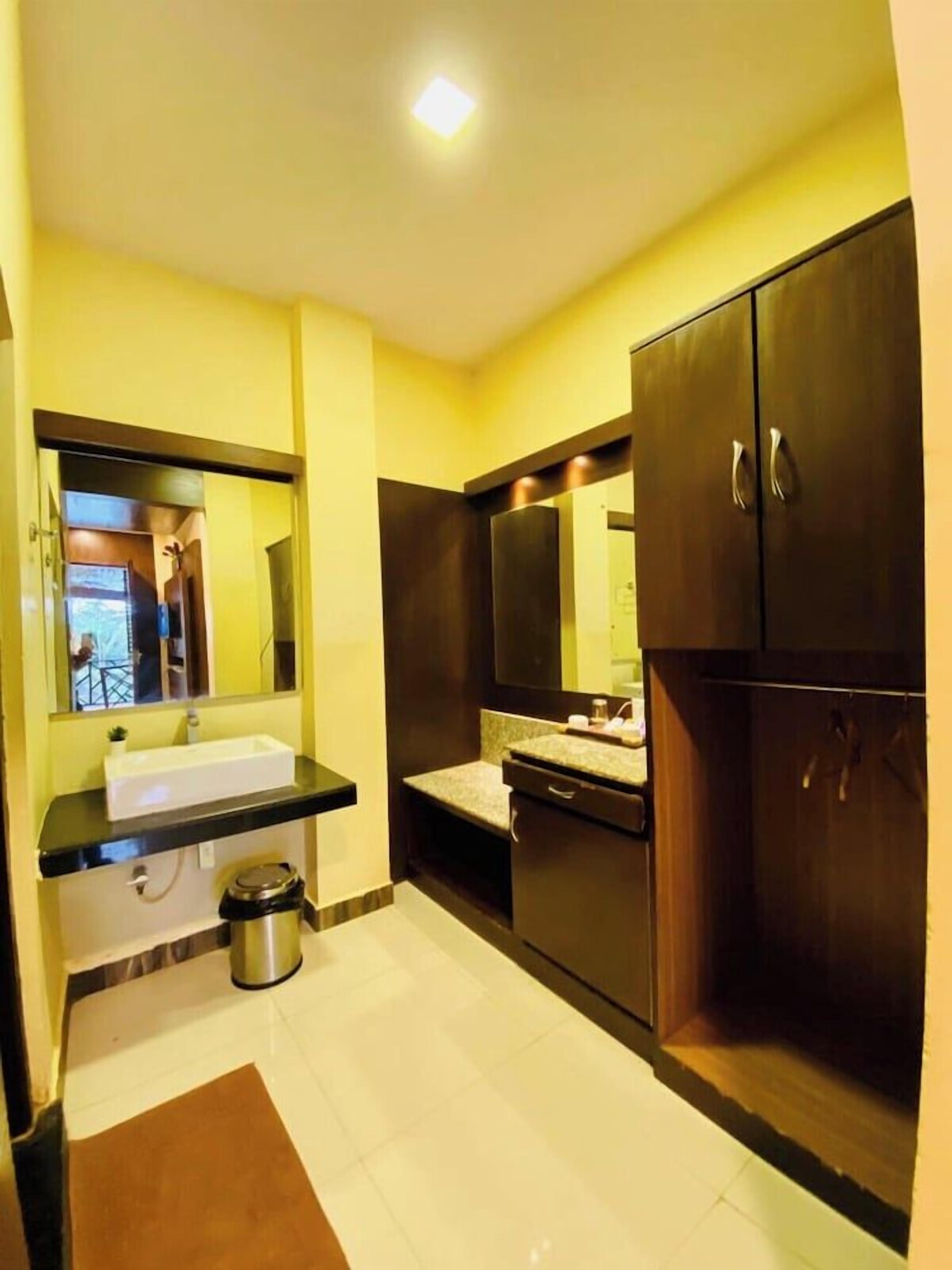 A bathroom with a sink, mirror, cabinets, and a trash bin.
