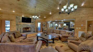 A spacious living room with a stone fireplace, leather sofas, a large coffee table, and a television mounted on the wall.