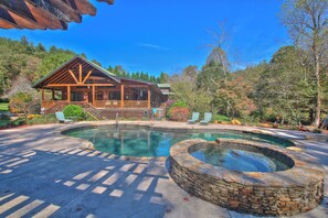 Una cabaña con fachada de madera, un jacuzzi de piedra y un área de piscina rodeada de árboles.
