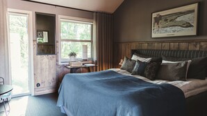 A bedroom with a large bed, a window with curtains, a framed picture on the wall, and a small table with a lamp. - Tweed Hotell Skaftö (Fiskebackskil)