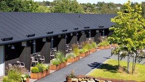 A building with a curved roof and multiple outdoor seating areas with chairs and planters. - Tweed Hotell Skaftö (Fiskebackskil)