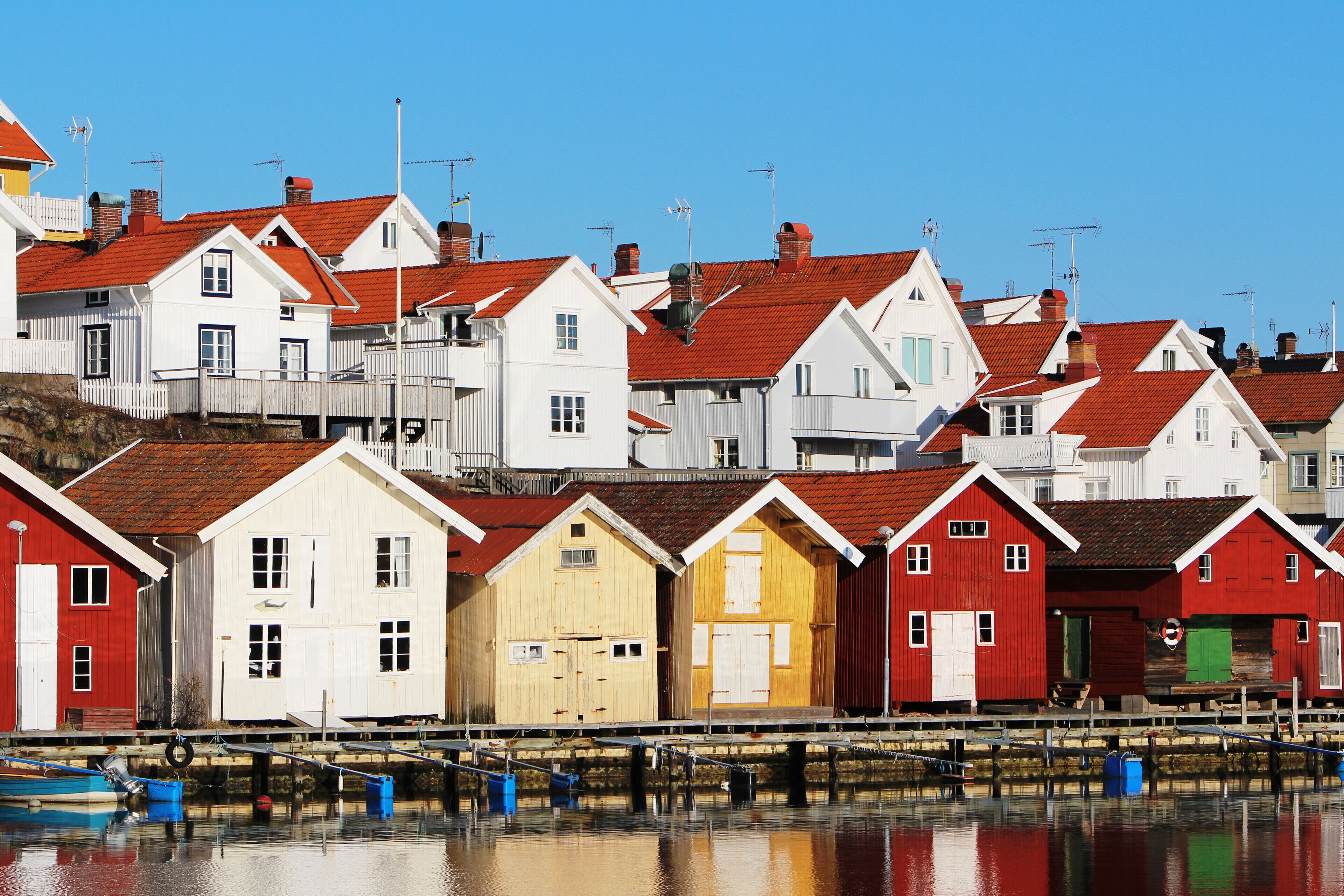 A row of colorful wooden buildings with red roofs, situated by a calm body of water.