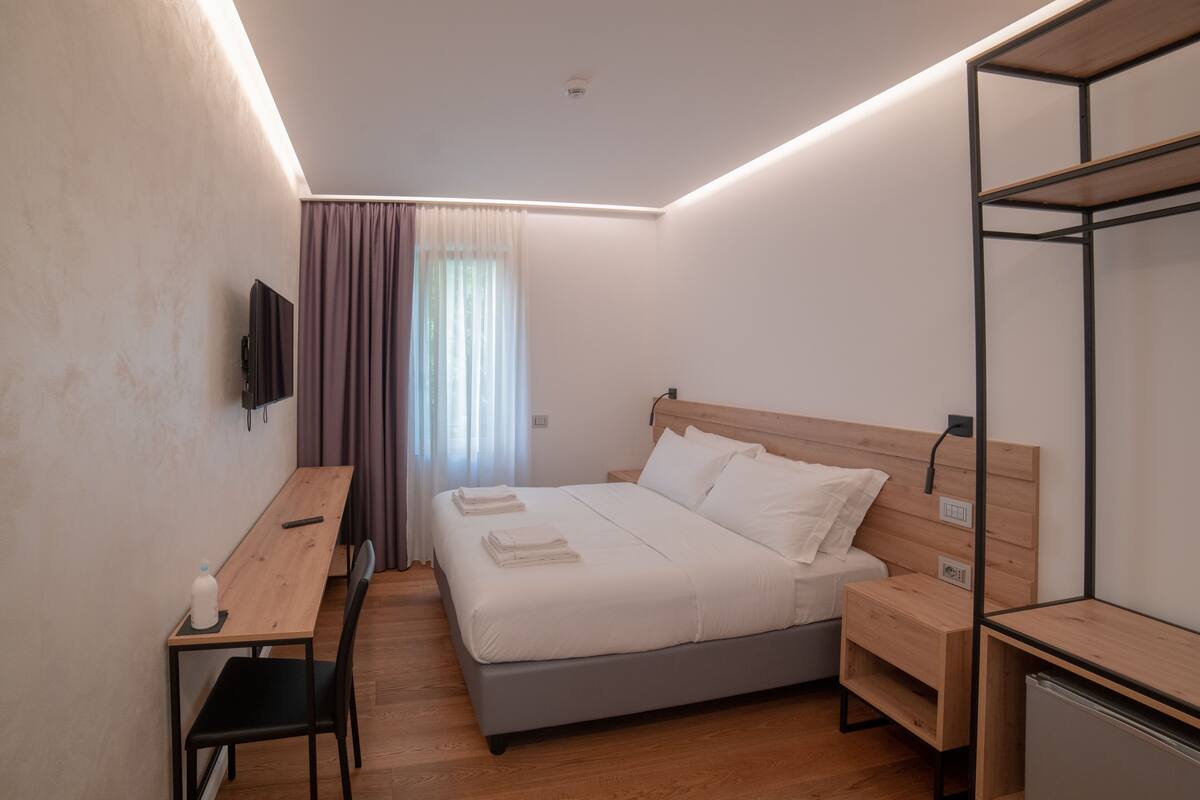 A modern bedroom with a bed, bedside tables, a desk, and a TV.
