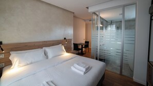 A modern hotel room with a large bed, a wooden headboard, a glass door closet, and a small table with chairs. - GRANDI 32  Boutique Residence (Segrate)