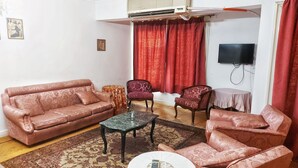 Ein Wohnzimmer mit einer Couch, zwei Sesseln, einem kleinen Tisch und einem an der Wand montierten Fernseher.