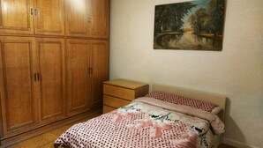 Ein Schlafzimmer mit einem Bett, einem Holzschrank, einem kleinen Nachttisch und einem Bild an der Wand.