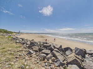 A beach with large rocks in the foreground, a sandy shore, and the ocean in the background.