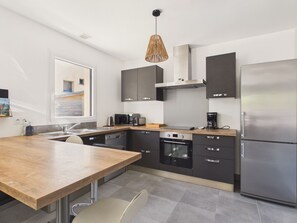 A modern kitchen with a wooden table, built-in appliances, and a large window.