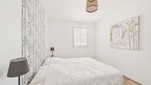 A minimalist bedroom with a bed, a lamp, a hanging light fixture, and a wall-mounted artwork.