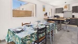 A modern kitchen with a dining area, large windows, and a view of the sky.