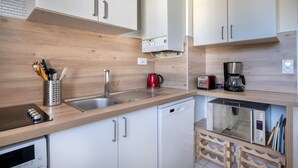 Una cucina moderna con mobili bianchi, lavello in acciaio inossidabile, bollitore rosso, macchina del caffè, forno a microonde ed elettrodomestici.