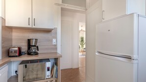 Una cucina compatta con mobili bianchi, un forno a microonde integrato, una macchina da caffè e un frigorifero bianco.