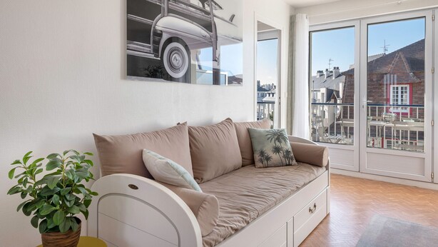 Un soggiorno moderno con un divano beige, una pianta in vaso e un'ampia finestra con vista sulla città.