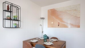Zona pranzo con tavolo in legno apparecchiato per quattro persone, una mensola in metallo con piante e un grande quadro astratto al muro.