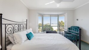 A bedroom with a bed, a chair, and a view of the outdoors through a window. - Dive into Dorset - 10 Dorset Court (CARRICKALINGA)